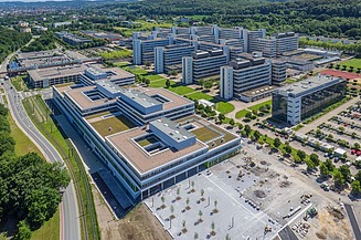 Universitätscampus von oben mit drei flachen Blocks und Parkplatz im Vordergrund und 5 riegelförmigen Bauten dahinter